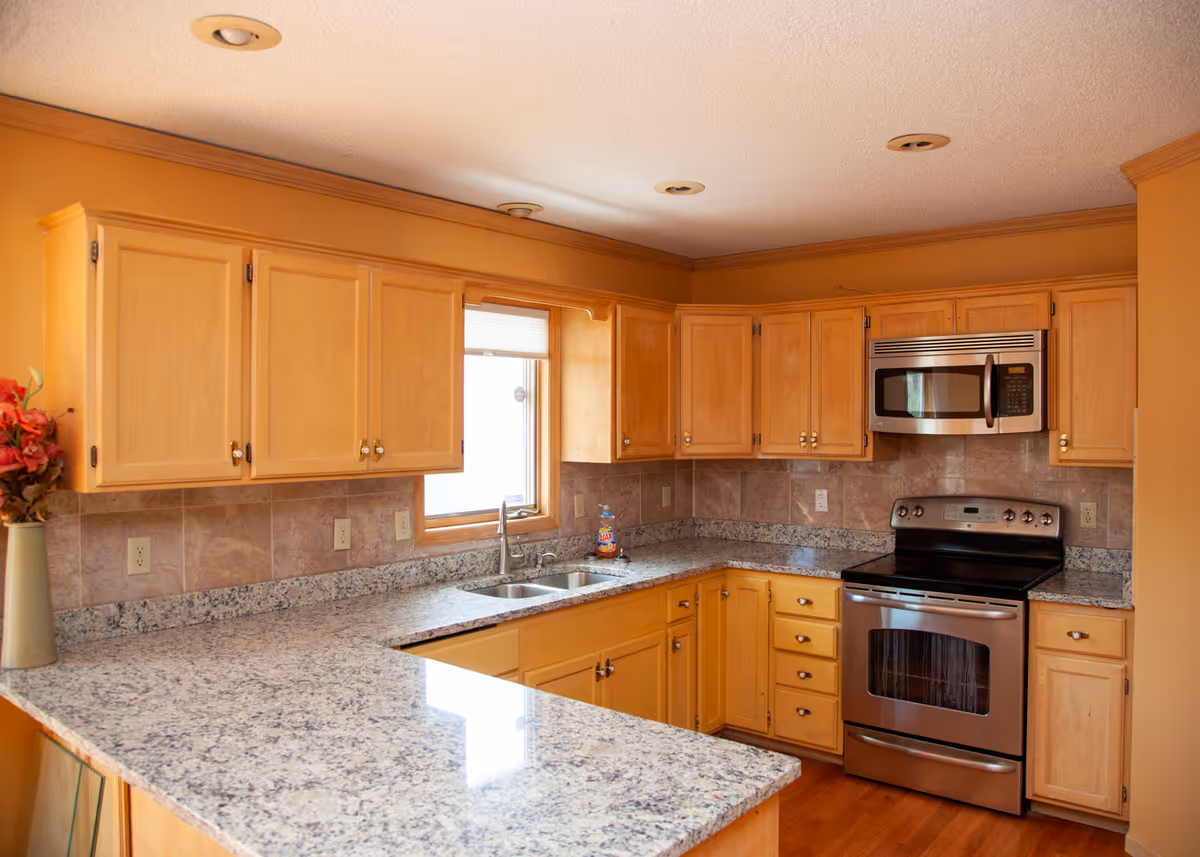 Sunny kitchen with granite countertops, light wood cabinets, stainless steel stove and microwave.