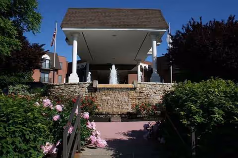 Front entrance of Kingswood Senior Living Community featuring a stone fountain and landscaped walkway.