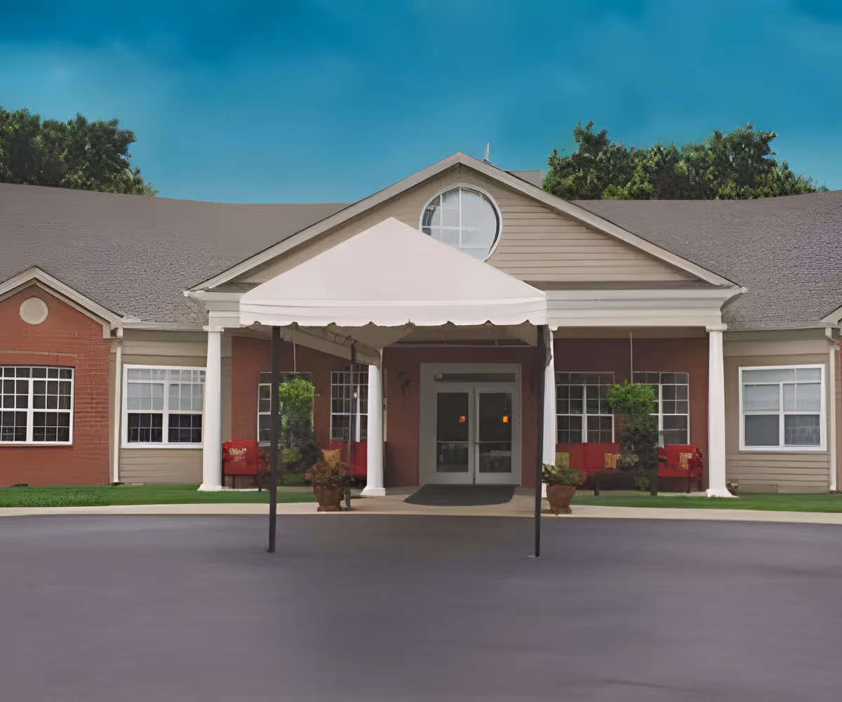 Front exterior view of Wilson Manor building with a covered entrance canopy, large windows, and a circular window above the entrance. There are potted plants and red chairs visible near the entrance.