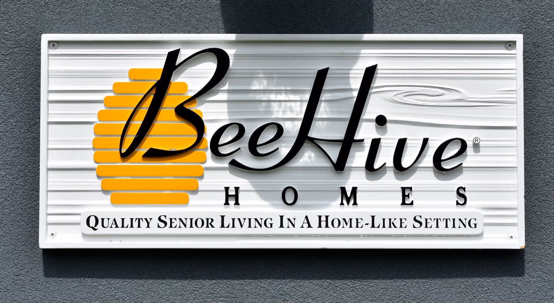 BeeHive Homes sign on a gray exterior wall advertising quality senior living.