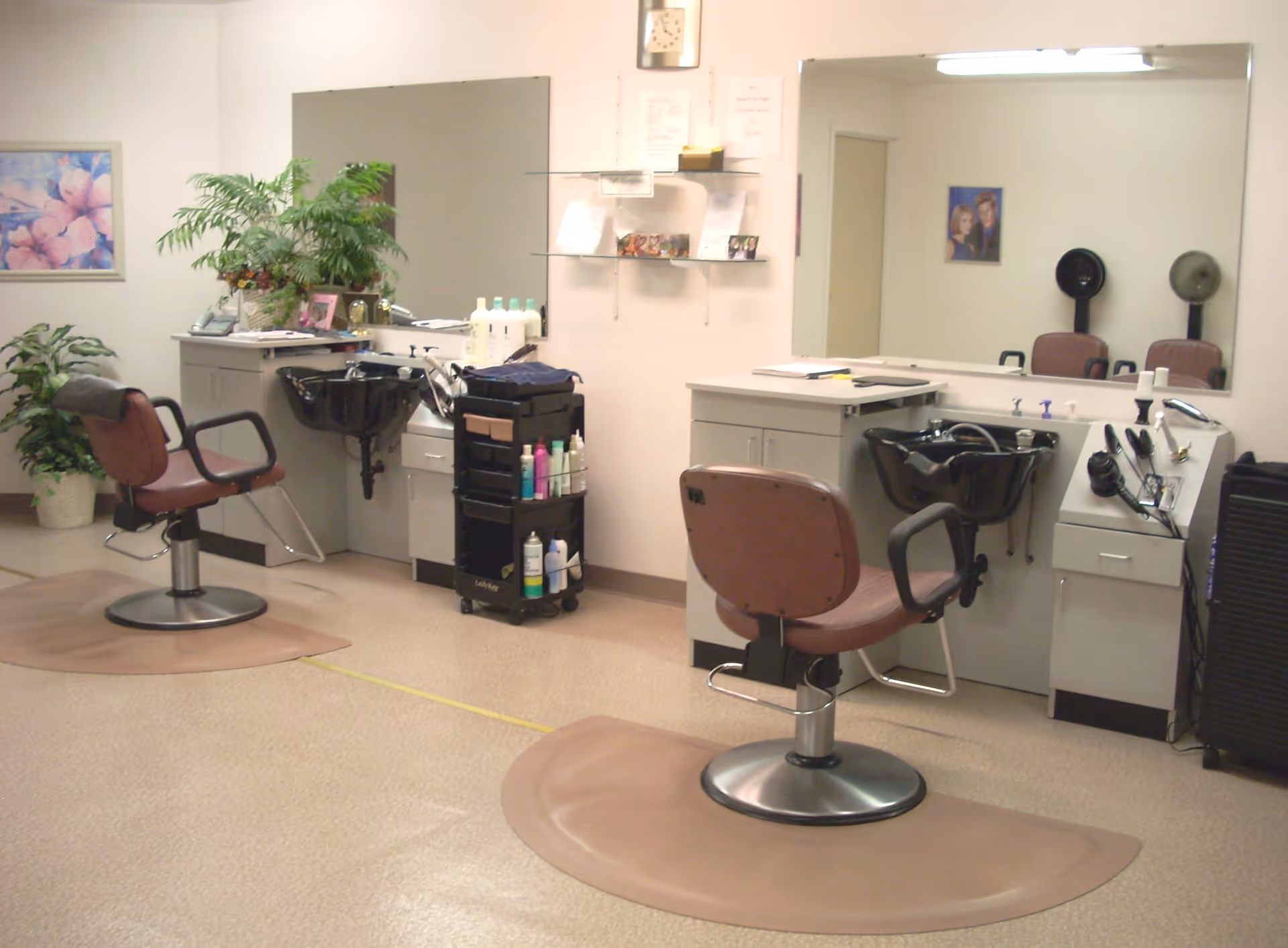 A small salon room with styling chairs, shampoo basins, large mirrors and shelving with hair products.