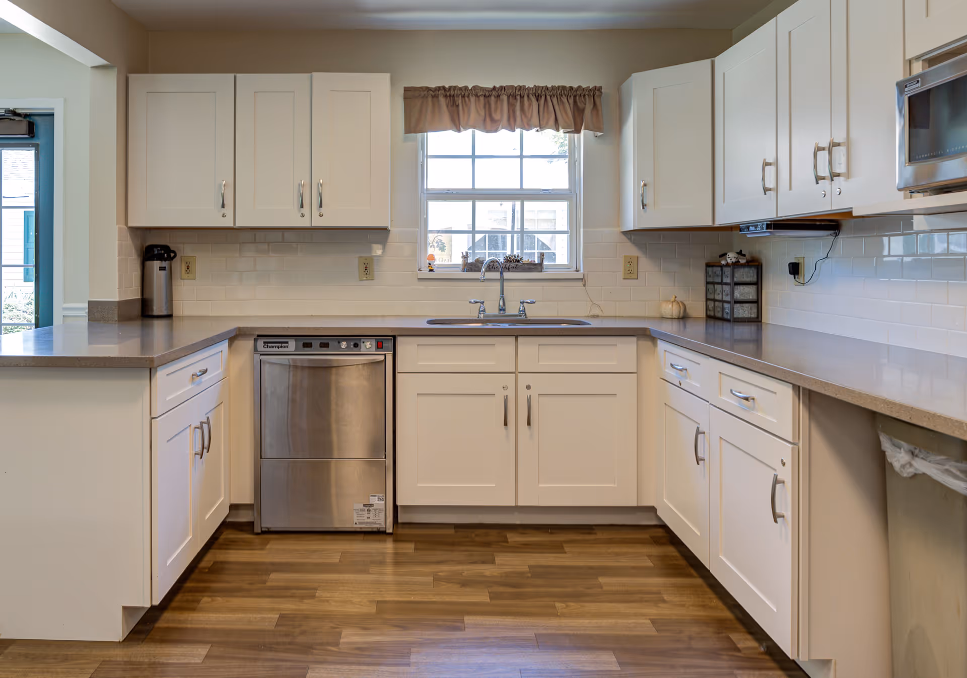 Bright kitchen with white cabinets, a stainless dishwasher, sink under a window, and wood-look flooring.