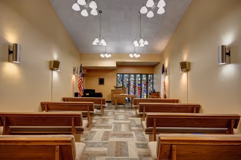 Small chapel-style interior with wooden pews facing an altar and stained-glass window.