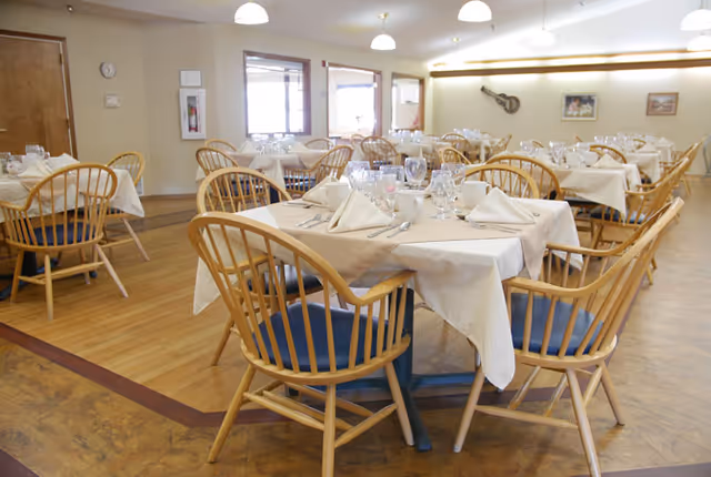 A dining room with multiple tables set with tablecloths, napkins, glassware, and wooden chairs.
