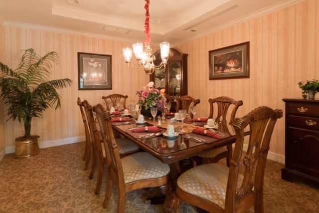 Formal dining room with a large wooden table set for a meal, ornate chairs, chandelier, and floral centerpiece.