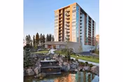 Multi-story senior living building with balconies overlooking landscaped grounds, a pond, and a small rock waterfall.