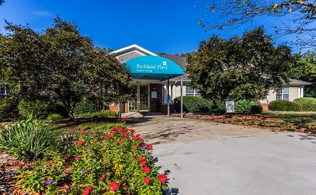 Exterior view of Richland Place Senior Living entrance with green awning, trees, and landscaping