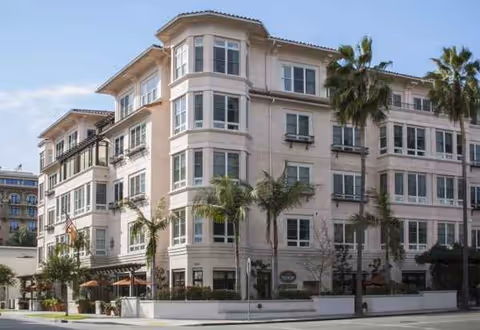 Exterior view of Sunrise of Beverly Hills senior living building with palm trees lining the street.