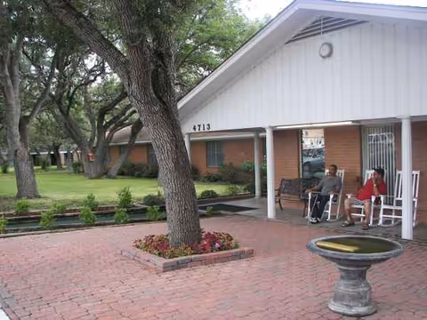 Exterior view of Hacienda Oaks Nursing and Rehabilitation Center with residents on a porch beneath trees.