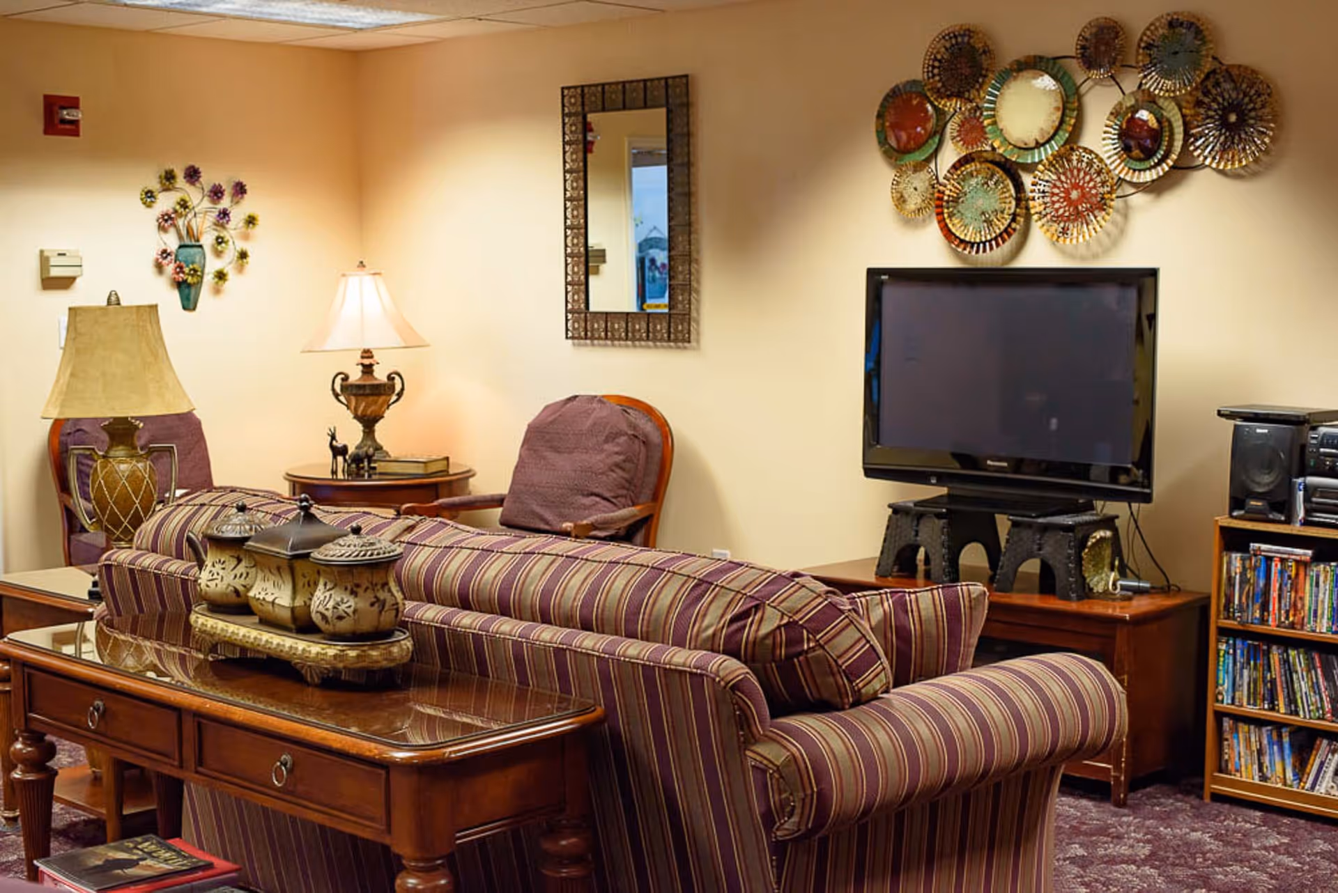 Cozy lounge with striped sofas facing a TV, side tables with lamps, decorative wall art, and a small media shelf.