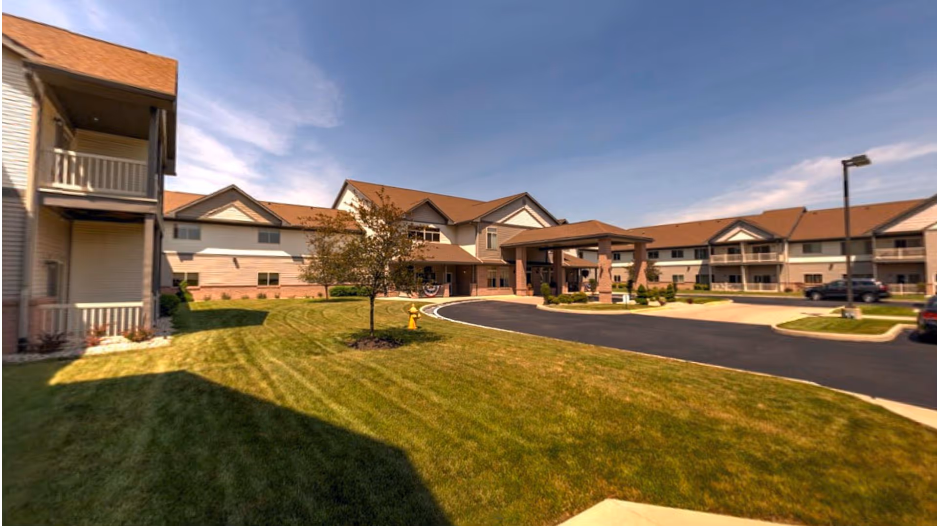 Front exterior of a multi‑story retirement community building with a covered entrance, landscaped lawn, and parking drive.