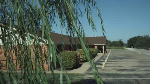 Front exterior of Concho Health and Rehabilitation Center with parking lot and overhanging branches.