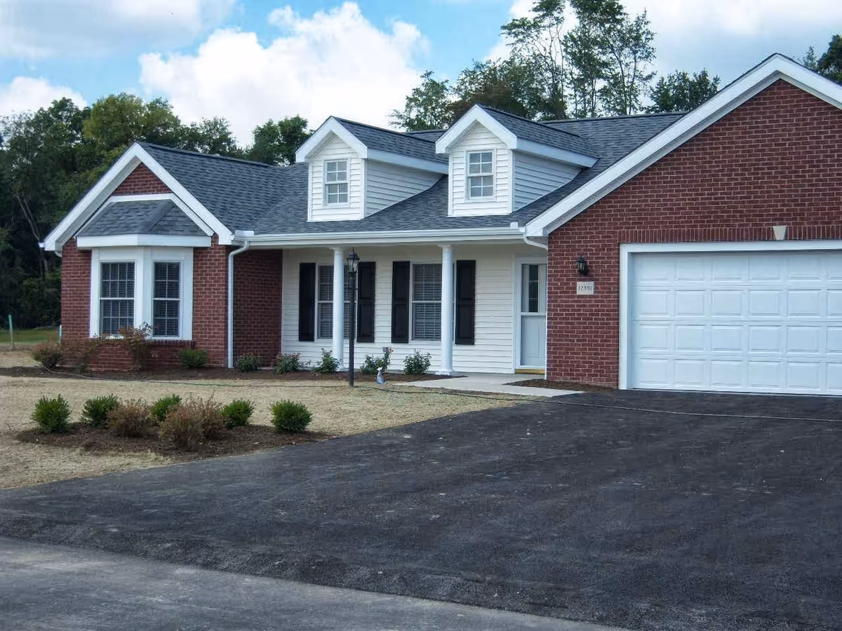 Single-story brick and siding house with an attached garage, front porch, dormer windows, and a paved driveway.