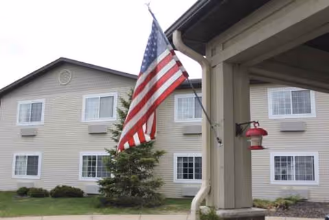 Exterior view of a beige senior living building with an American flag near the entrance.