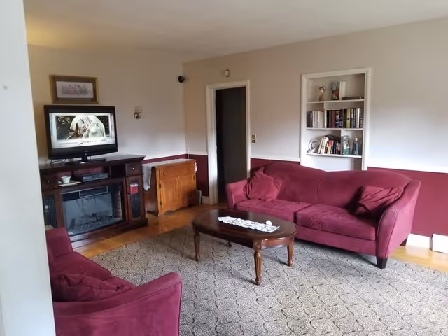 Cozy living room with burgundy sofas, a wooden coffee table, TV on a stand, built-in bookshelf, and patterned area rug.