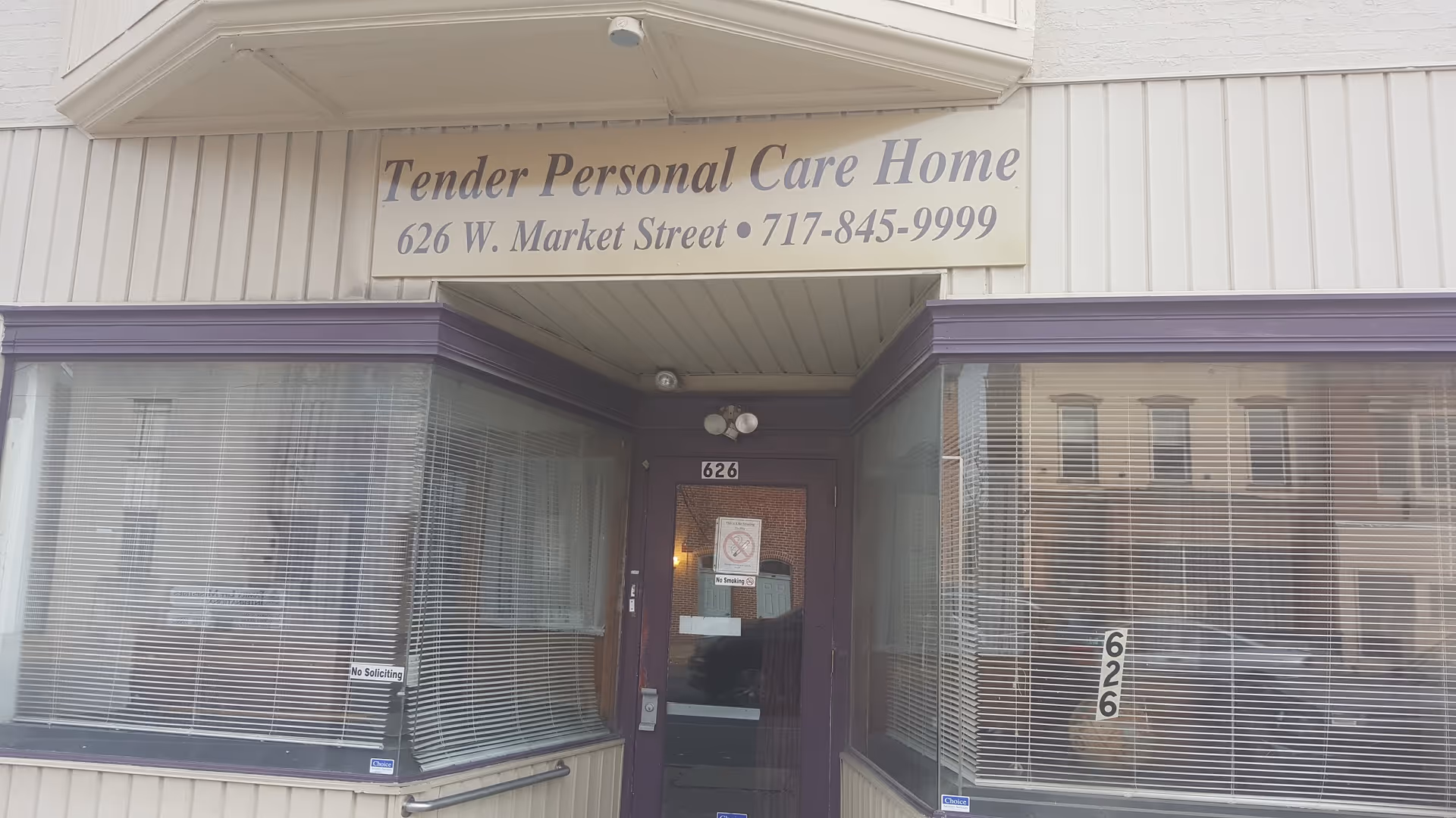 Street-level entrance of Tender Personal Care Home with a sign above the door and large display windows on either side.
