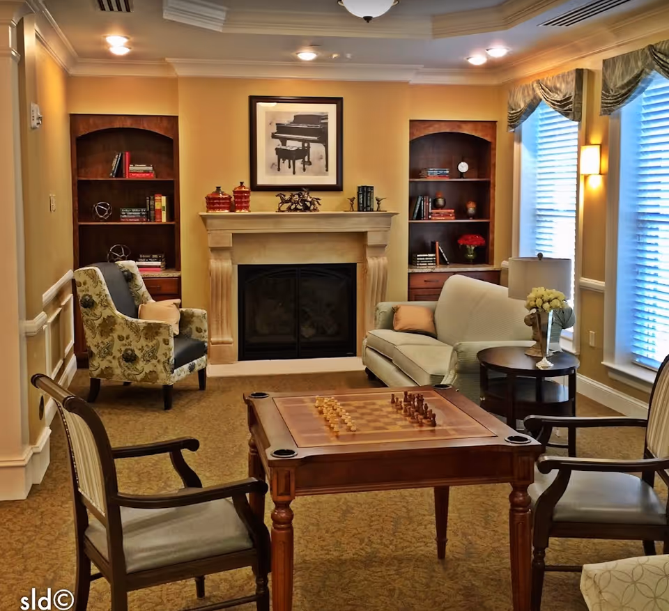 Cozy living room with a fireplace flanked by bookshelves, sofas and chairs around a central chess table.