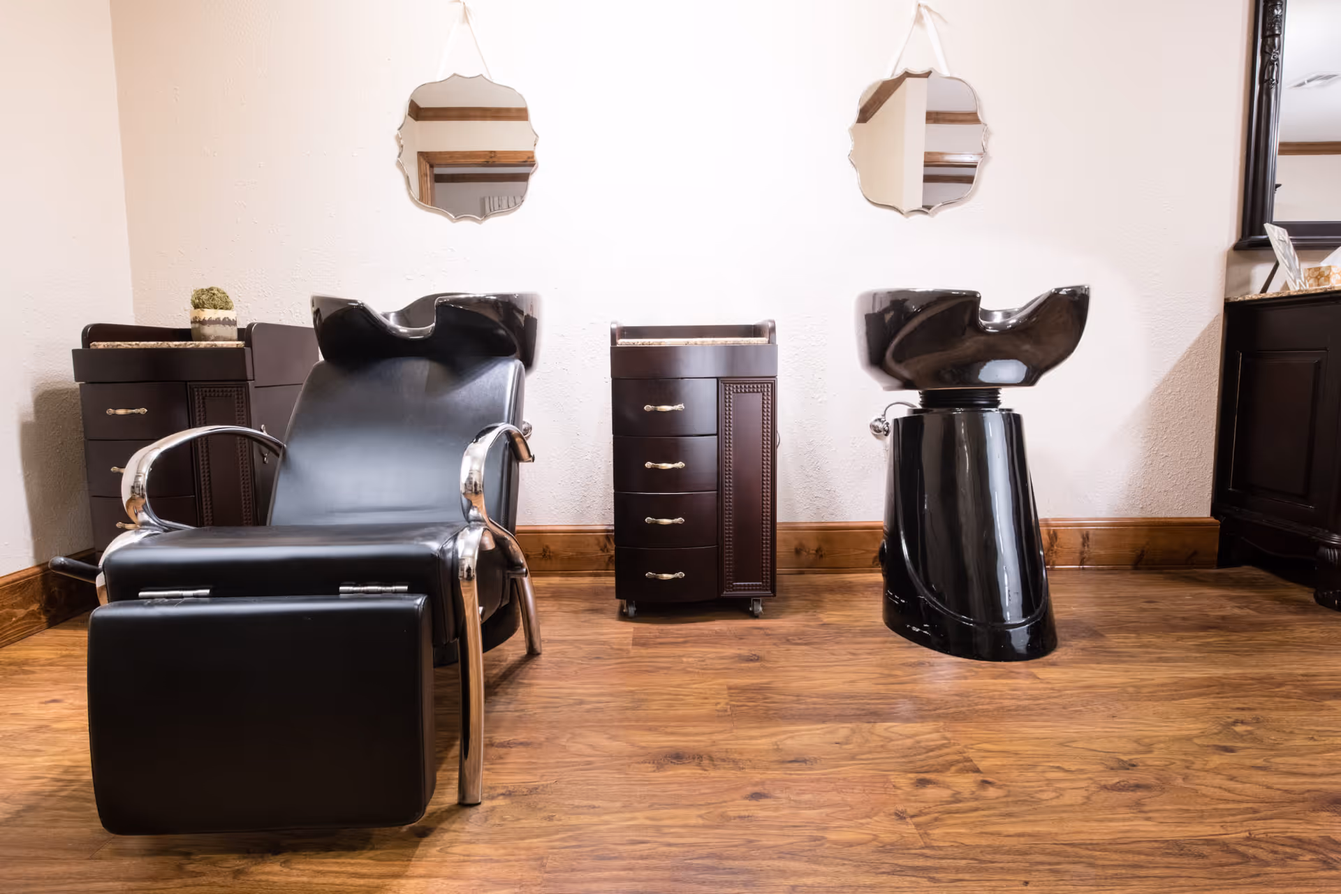 Interior salon area with a black reclining shampoo chair, a black wash basin, and dark wood cabinets on a hardwood floor.