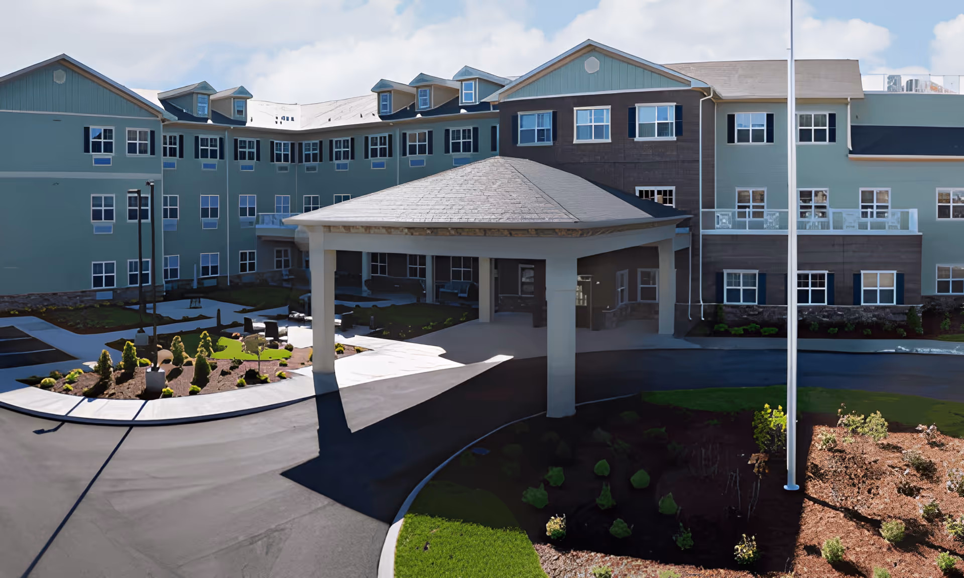 The entrance facade of Jubilee House, featuring a covered portico and landscaped garden area with shrubs and seating.