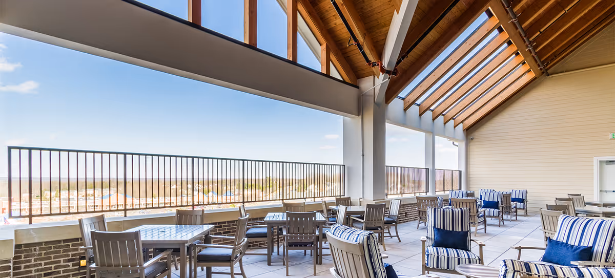 Covered rooftop patio with tables and striped cushioned chairs under a wood-beamed roof overlooking a distant view.