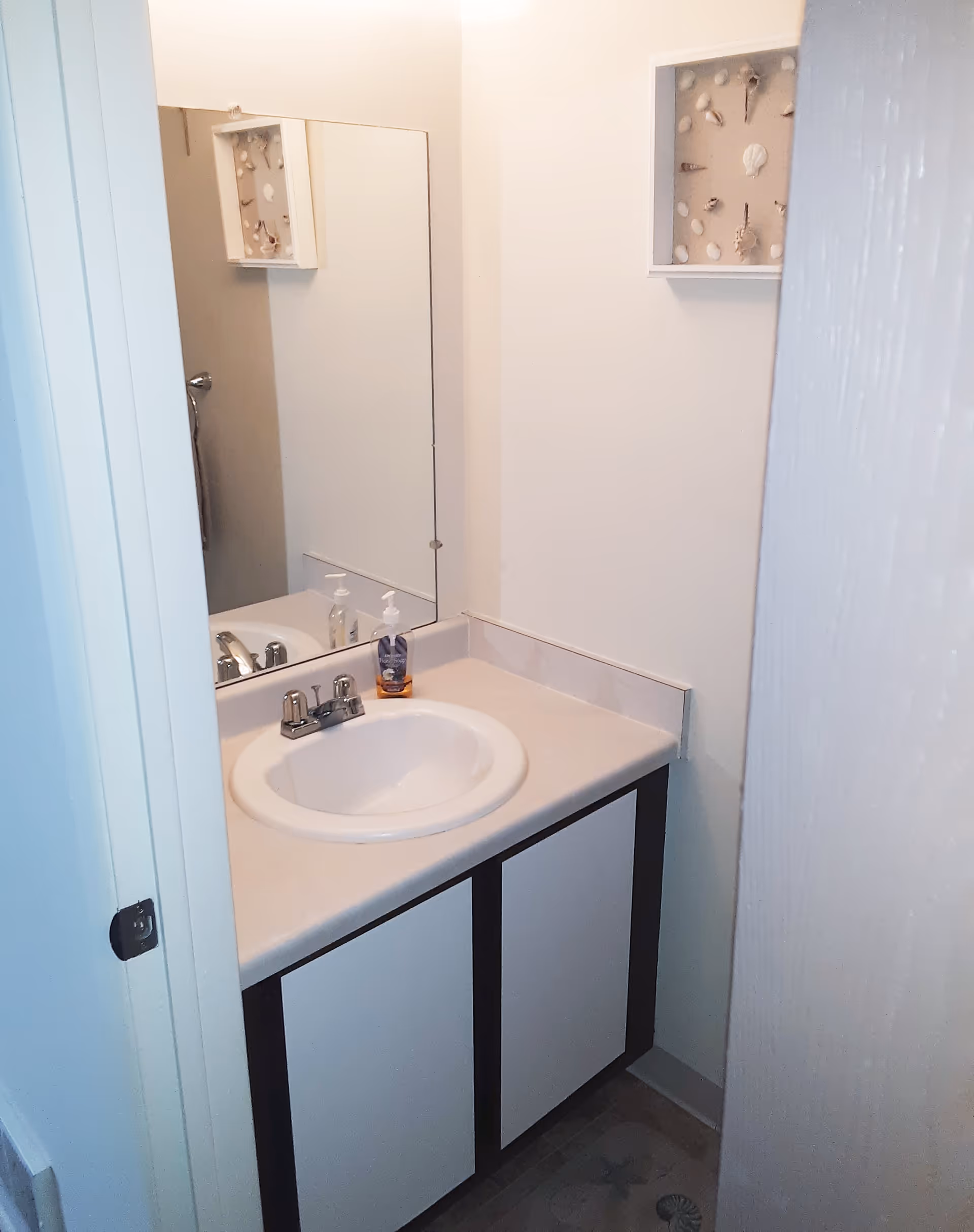 Compact bathroom vanity with a round sink, faucet, mirror, and small wall decor box.