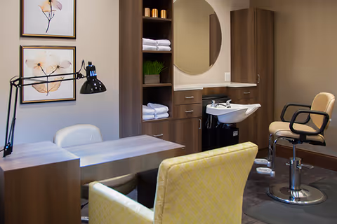 Salon-style interior with styling chairs, a shampoo sink, wooden cabinetry, and a small desk.