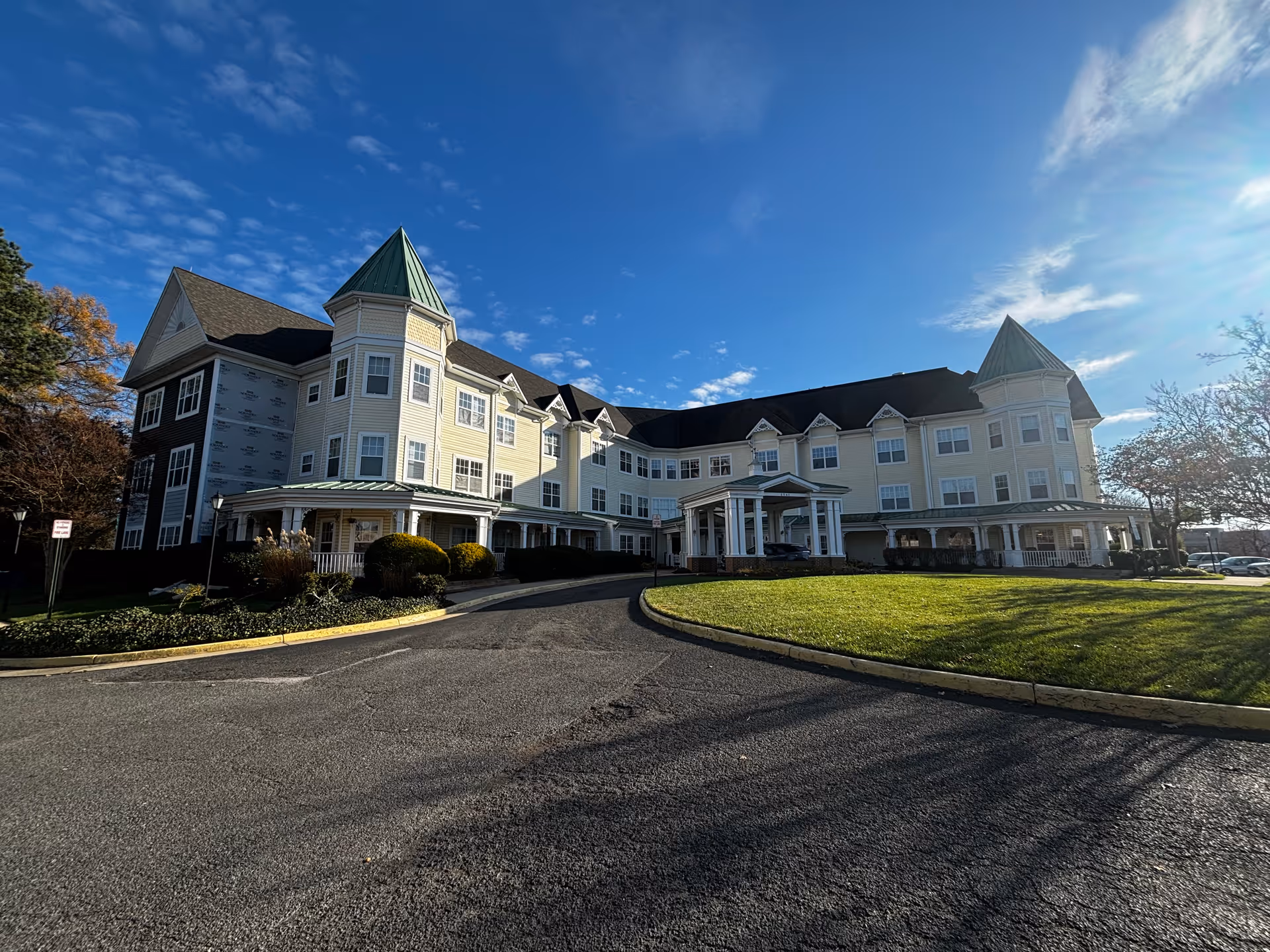Large three-story residential building with turrets, a covered entrance and circular driveway under a blue sky.