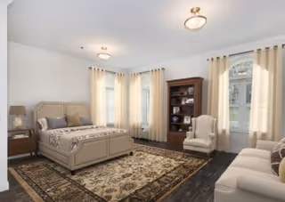 Spacious furnished bedroom with a bed, patterned area rug, armchair, bookcase, and windows with curtains.