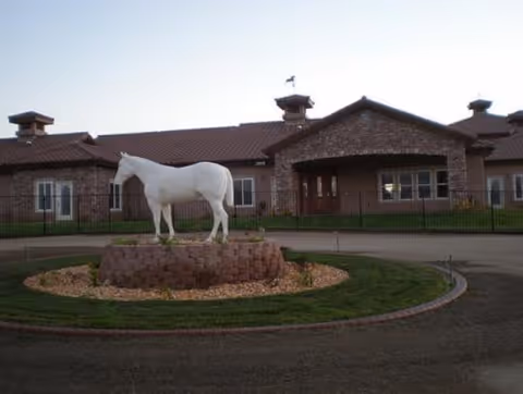 A white horse statue sits on a brick pedestal near the entrance of a brick building.