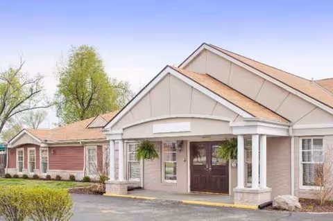 Exterior view of a single-story senior living facility entrance with porch and landscaping