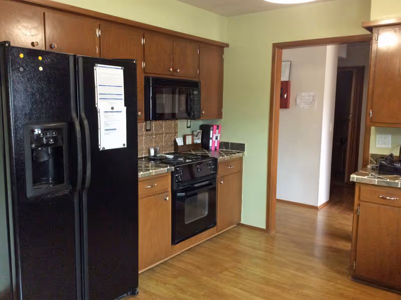 Kitchen featuring a black refrigerator, black oven and microwave, wood cabinets, tiled countertops, and laminate wood flooring.