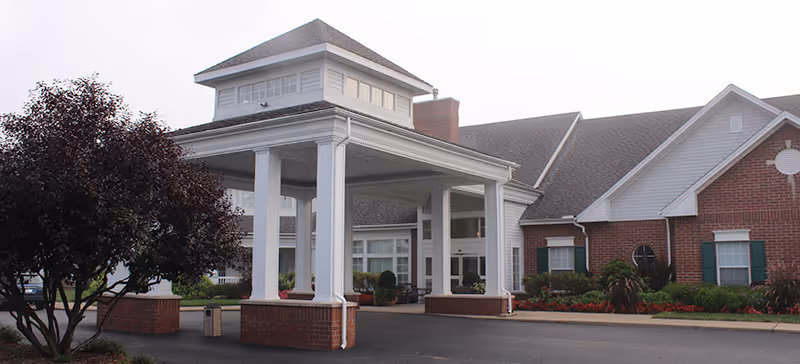 Front entrance canopy and facade of The Glenwood Community building with white columns, brick walls, and landscaping.
