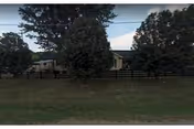Exterior view of a single-story Hartsville Health and Rehab building behind a wooden fence with trees.