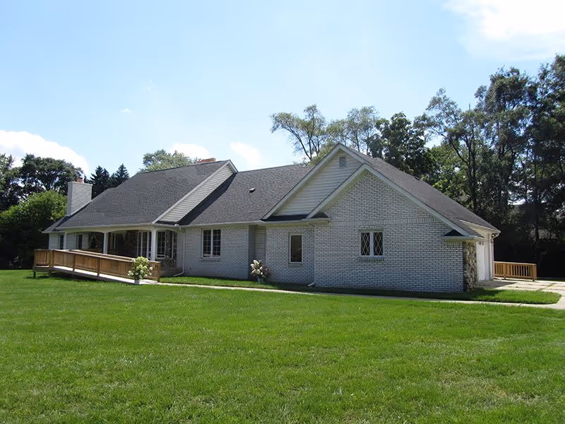 White brick, single-story building with a green lawn and wooden ramp.