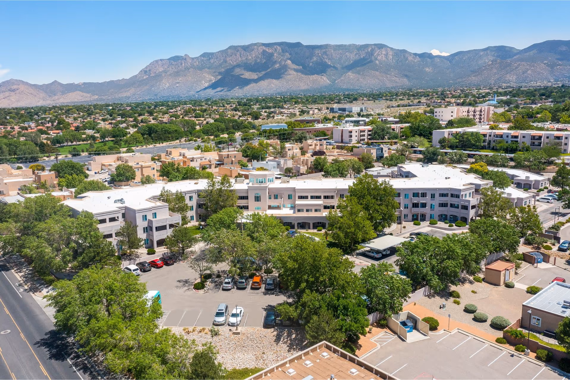 Aerial view of the Bear Canyon Estates Sky Active Living senior living campus with buildings, parking lot, surrounding trees, and mountains in the background.