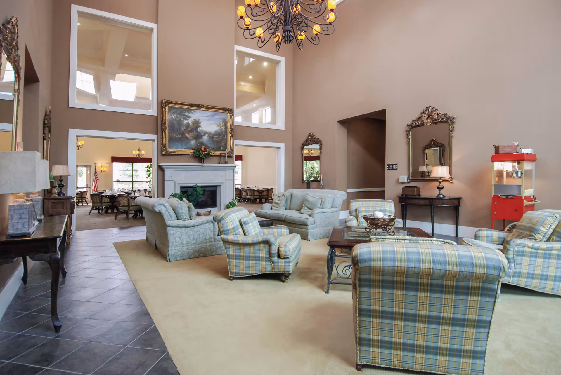 Spacious senior living common room with high ceilings, sofas and armchairs arranged around a fireplace and coffee table.