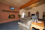 Cozy living room with a brick fireplace, TV, sofas, and wooden ceiling beams.