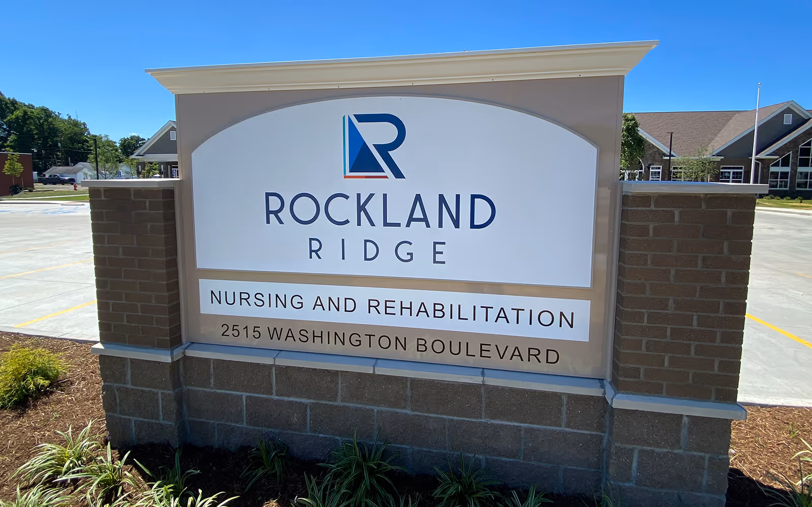 Outdoor sign for Rockland Ridge Nursing and Rehabilitation located at 2515 Washington Boulevard, with a parking lot and building visible in the background under a clear blue sky.