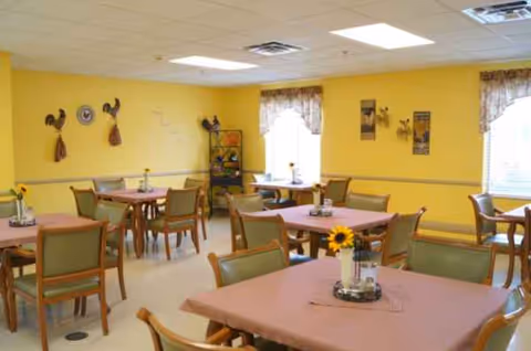 Bright yellow dining room with pink-tablecloth tables and sunflowers in vases.