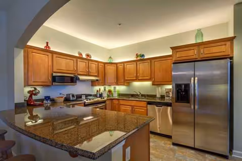 Open-concept kitchen with granite island, wood cabinets, and stainless steel appliances.