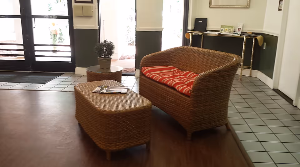 Lobby seating area with a wicker loveseat and ottoman near glass entry doors.