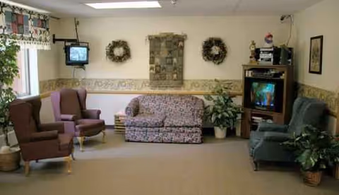 Cozy senior living room with chairs, a floral sofa, plants, and wall decor.