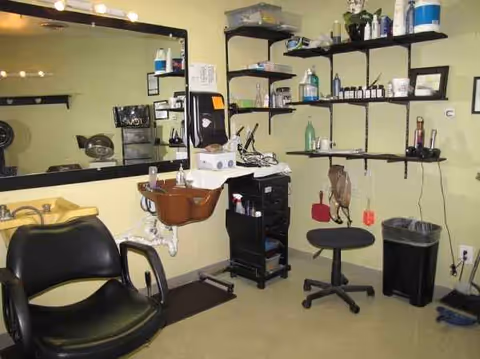 Interior of a senior living facility hair salon with chair, sink, and shelves.