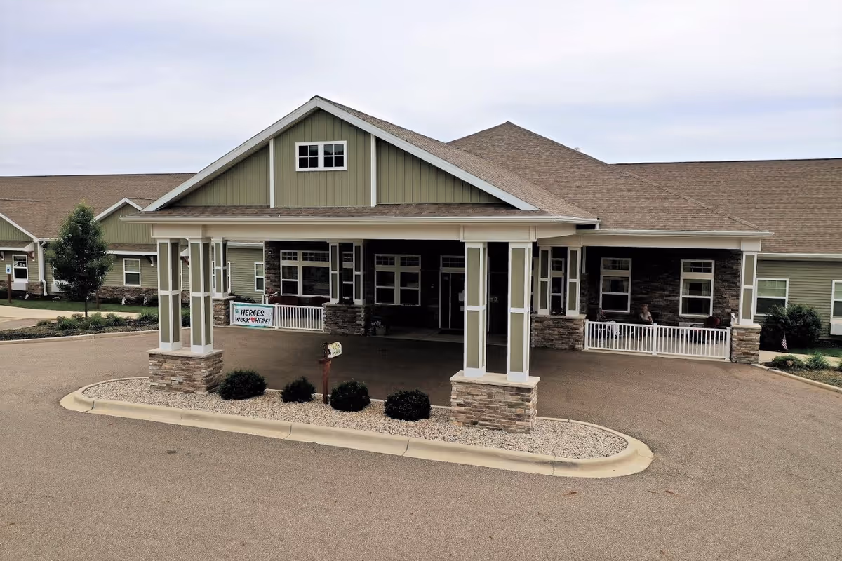 Front entrance of a single-story senior living building with a covered porte-cochere, columns, and a driveway.