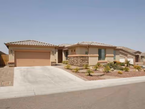 Front exterior of a single-story beige building with a two-car garage and desert landscaping.