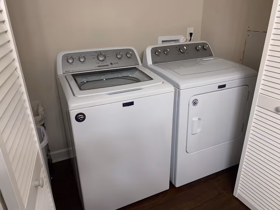 A white top-loading washing machine and matching dryer side by side in a small laundry closet.