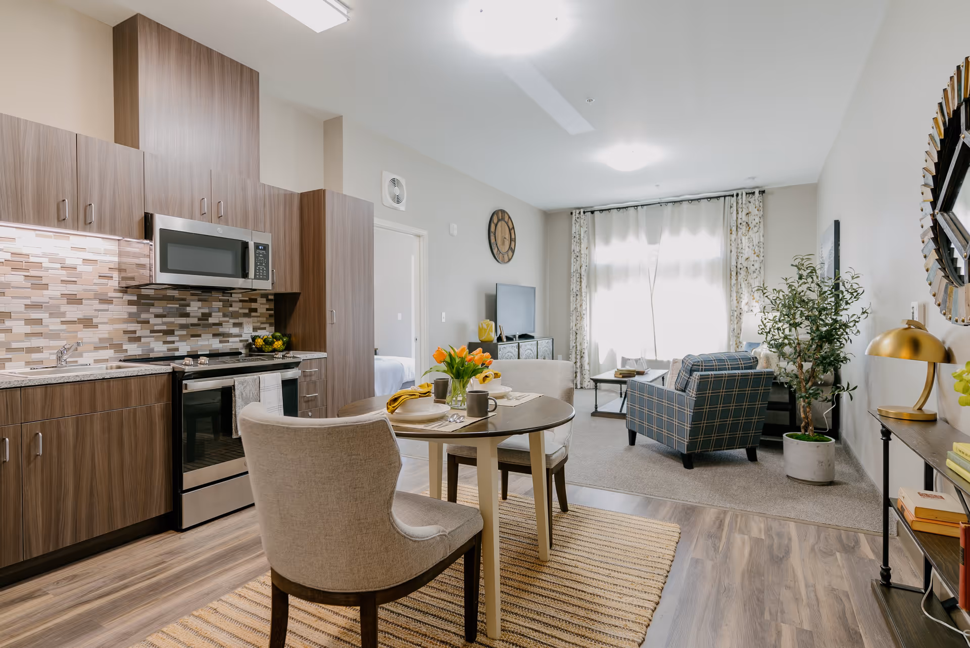 Open-concept interior showing a modern kitchenette, round dining table, and a cozy living area with armchairs and a TV.