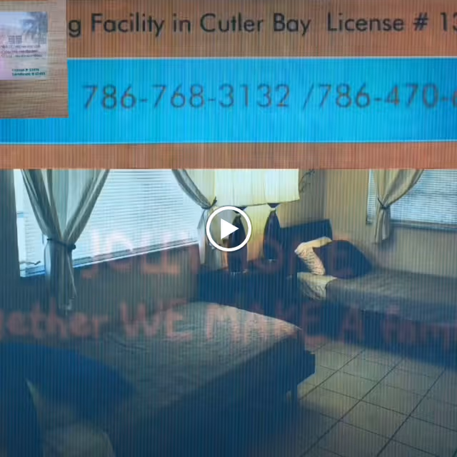 A bedroom with two single beds, each with pillows and blankets. There is a nightstand with a lamp between the beds. The room has tiled flooring and windows with curtains allowing natural light to enter.