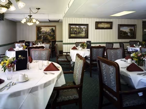 Dining room with round tables set with white tablecloths, folded napkins, floral centerpieces, and upholstered chairs.