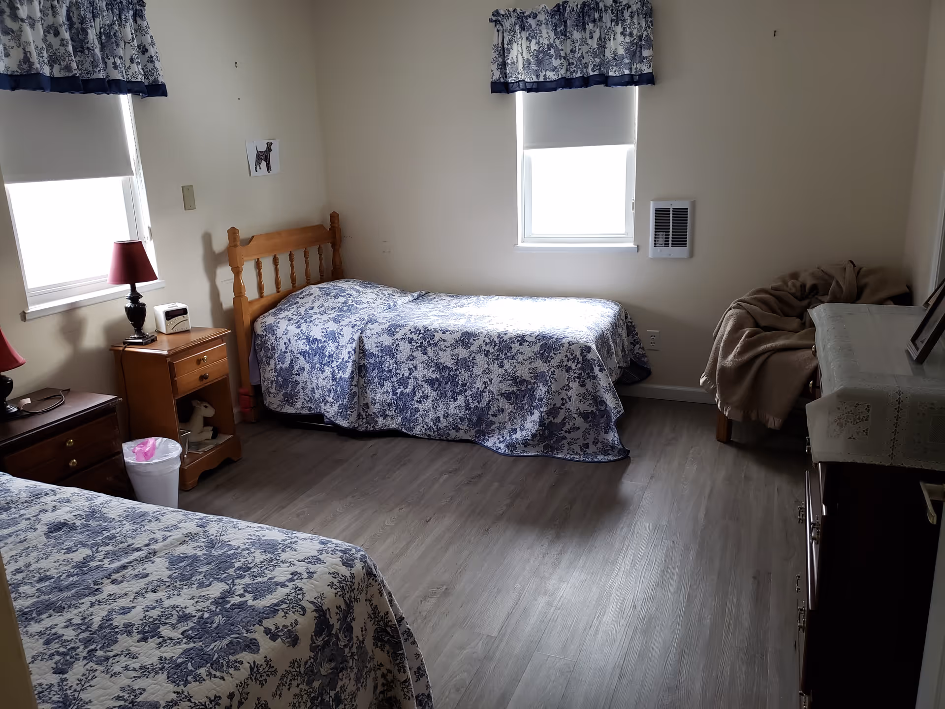 A small bedroom with two blue floral quilts, nightstands, and windows.